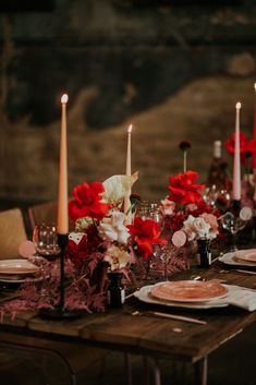 the table is set with red and white flowers, candles, and wine glasses on it