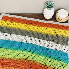 a multicolored crocheted blanket sitting on top of a wooden table next to a potted plant