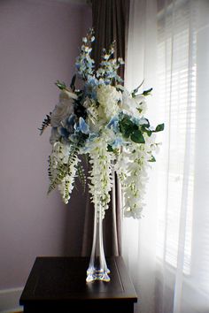 a vase filled with white and blue flowers sitting on top of a table next to a window