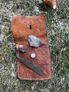 an old leather wallet with some tools in it laying on the ground next to a rock