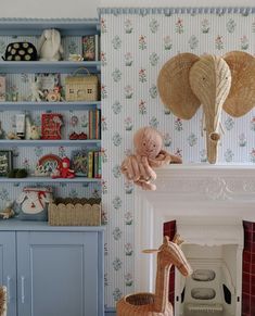 a stuffed giraffe sitting next to a fireplace in a room with wallpaper