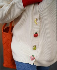 a close up of a person wearing a sweater and holding a purse with strawberries on it