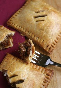 two pieces of meat filled pastries on a wooden cutting board with a fork next to them