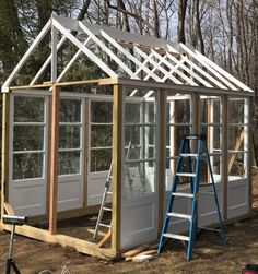 a house being built in the woods with windows on each side and ladders attached to it