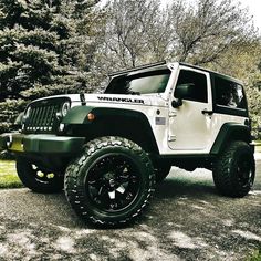 a white and black jeep is parked on the side of the road in front of some trees