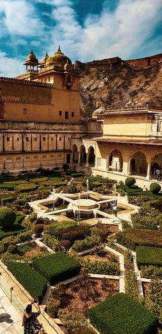 a person standing in front of a large building with many plants and bushes around it