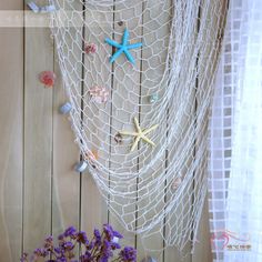 there is a white net with starfishs on it and purple flowers in the vase