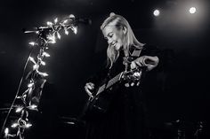 a black and white photo of a woman playing an electric guitar in front of a microphone