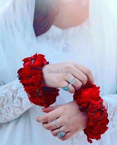 a woman in white wedding dress holding red flowers with her hands and ring on the wrist