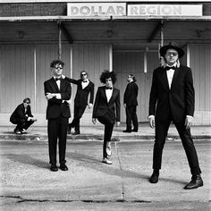 black and white photograph of men in tuxedos standing on the sidewalk outside a building