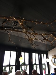 people sitting at tables in front of large windows with christmas lights hanging from the ceiling