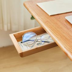 a pair of glasses sitting in a drawer on top of a desk next to a laptop computer