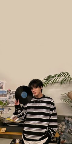 a young man holding a record in his right hand while standing next to a plant