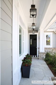 a black door is on the side of a white house with two planters in front