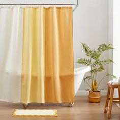 a yellow and white shower curtain sitting next to a bath tub in a room with wooden floors