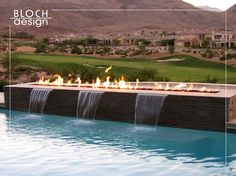 a fire pit in the middle of a pool with water running down it and mountains in the background