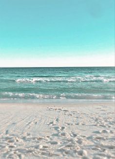 the beach has footprints in the sand near the water and blue sky above it is an ocean view