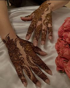 two hands with henna designs on them sitting next to pink flowers and bouquets