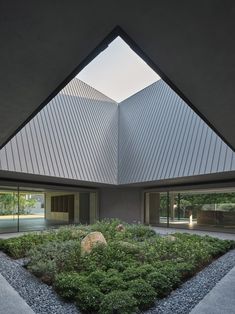 an open courtyard with plants and rocks in the foreground, under a triangular roof