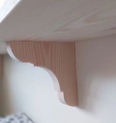 a close up of a wooden shelf on a wall with a bed in the background