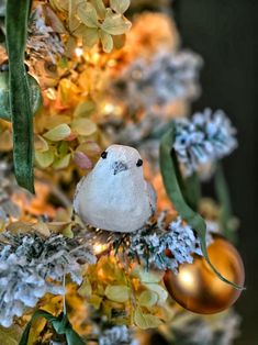 a white bird sitting on top of a christmas tree with ornaments hanging from it's branches