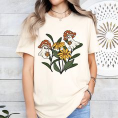 Embrace your love for the whimsical with this unique T-shirt featuring adorable mushroom ghosts nestled among vibrant flowers. Perfect for fantasy and nature enthusiasts, this graphic tee boasts a playful and charming design that is sure to capture the imagination. Crafted from soft, breathable fabric, it's designed for both comfort and style, making it an ideal gift or addition to your casual wardrobe. Whether you're heading out for a day in the park or just lounging at home, this shirt is the perfect way to add a touch of enchantment to your outfit. This classic unisex jersey short sleeve tee fits like a well-loved favorite. These t-shirts have-ribbed knit collars to bolster shaping. The shoulders are tapered for a better fit over time. Dual side seams hold the garment's shape for longer Spring Mushroom Print Graphic Tee, Spring Crew Neck T-shirt With Mushroom Print, Spring Mushroom Print Crew Neck T-shirt, Spring Mushroom Print Short Sleeve T-shirt, White Short Sleeve T-shirt With Mushroom Design, White Mushroom Print Short Sleeve Top, White Short Sleeve Tops With Mushroom Print, White Short Sleeve Top With Mushroom Print, Whimsical Cotton Short Sleeve Tops