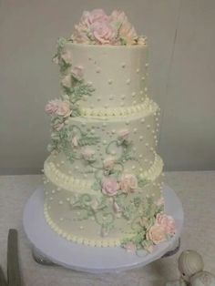 a three tiered wedding cake with pink flowers and pearls on the top, sitting on a table next to silverware