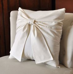 a white pillow with a large bow on it's back sitting on a couch