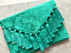 This one of a kind envelope clutch is a handmade bag featuring embroidered and a vibrant floral design. This is the perfect everyday accessory that will add color & joy to your style! Please note you will receive a clutch in the same color as pictured, however, it may have a different floral design as each one is one of a kind. The clutch includes a crossbody strap for hands-free style. Secure your belongings with a magnetic snap and full-length zipper featured in the black-lined interior. All i Summer Clutch Bag, Embroidered Clutch Bag, Summer Clutch, Embroidered Clutch, Steampunk Accessories, Embroidery Bags, Envelope Clutch, Free Style, Handmade Bag