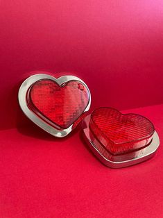 two heart shaped tins sitting on top of a red surface