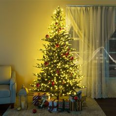 a lit christmas tree in front of a window with presents on the floor next to it