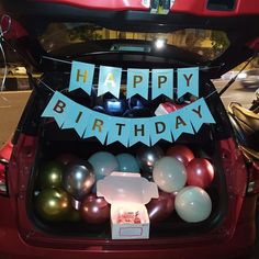 the trunk of a red car with balloons in it and a happy birthday banner on top