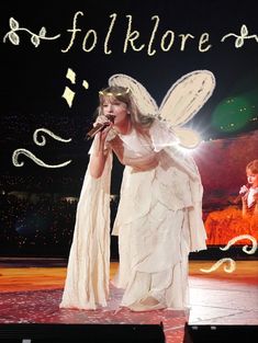 a woman in white dress on stage with angel wings and halo around her head holding a microphone