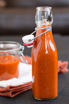 a glass bottle filled with sauce sitting on top of a table next to a cloth