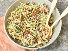 a bowl filled with shredded broccoli and carrots next to a wooden spoon