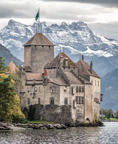 an old castle sitting on top of a body of water next to snow covered mountains