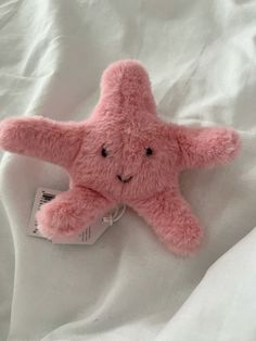 a pink starfish stuffed animal laying on top of a white bed sheet with a tag hanging from it's side