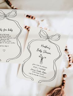 two wedding cards with bows on them sitting on a bed next to beads and beaded necklaces