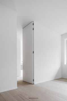 an empty room with white walls and wood flooring in the foreground is a window