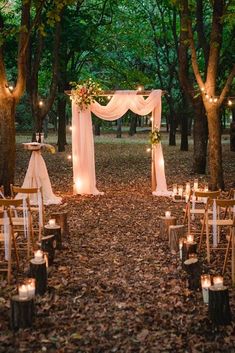 an outdoor wedding setup with candles and draping on the trees, surrounded by leaves