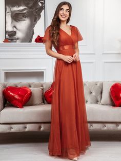 a woman standing in front of a couch wearing an orange dress