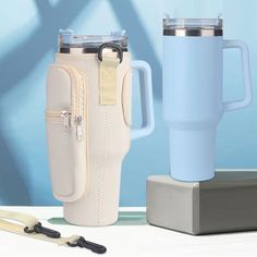 two travel mugs are sitting next to each other on a table with a blue wall in the background