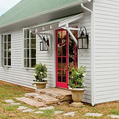 a small white house with a red door and two potted plants on the front porch