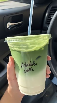 a hand holding a green drink in front of a steering wheel with the word matcha latte written on it