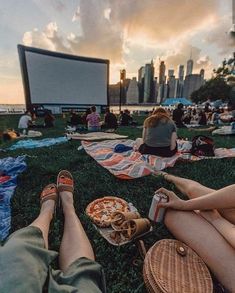 people are sitting on the grass watching movies and eating pizza in front of an outdoor movie screen