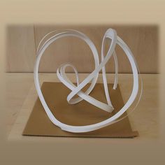 a sculpture made out of white paper on top of a cardboard box with a ribbon in the shape of a heart