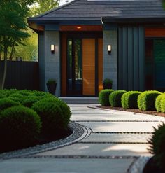 the front entrance to a modern home surrounded by greenery and shrubs with lights on