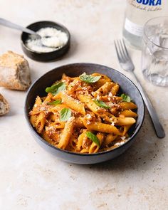 a black bowl filled with pasta and sauce next to bread on a white counter top