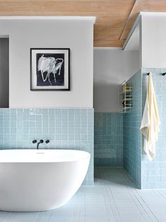 a white bath tub sitting next to a blue tiled wall in front of a painting