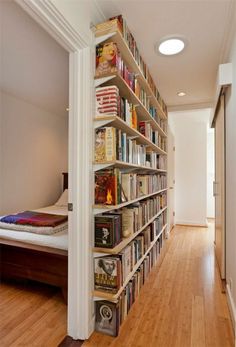 a book shelf filled with lots of books on top of a hard wood floor next to a bed